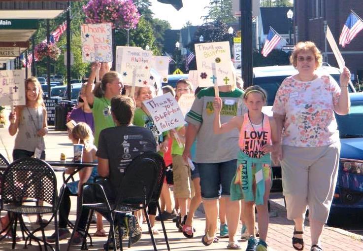 Melinda Estell and Steve Yoder lead a group of children down Main Street as they carried signs thanking community workers for their service.