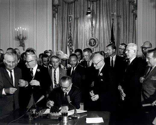 looks on as President Lyndon Johnson signs the Civil Rights