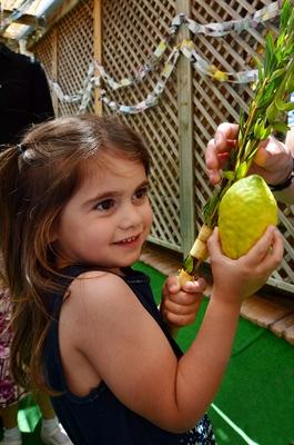A Jewish girl in a sukkah learns how to hold the Four species.
