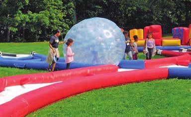 Children take turns inside a large inflated plastic ball and, with help, try to work their way along the inflatable track.