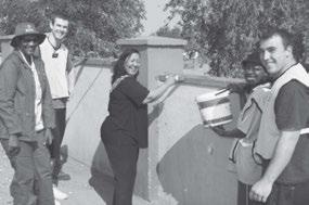 Windhoek Mayor Elaine Trepper paints a portion of the Katutura Cemetery wall while missionaries and others look on.