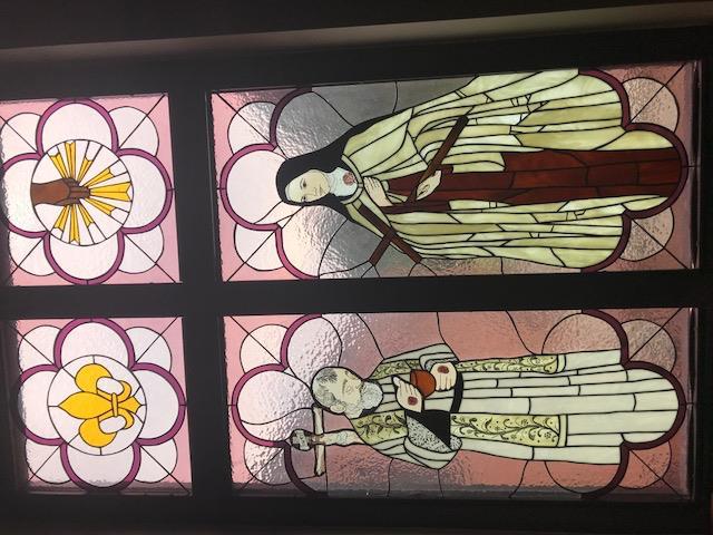 The first window on the left represents the spiritual work of mercy: Pray for the Living and the Dead. On the left St.