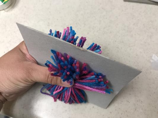 Cut through the bundle of yarn halfway between the two ties, to form two pompoms.