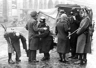 Give two things you can infer from Source A about the police state. Source A. German citizens being searched in the street by gestapo officers and armed uniformed police, 1933.