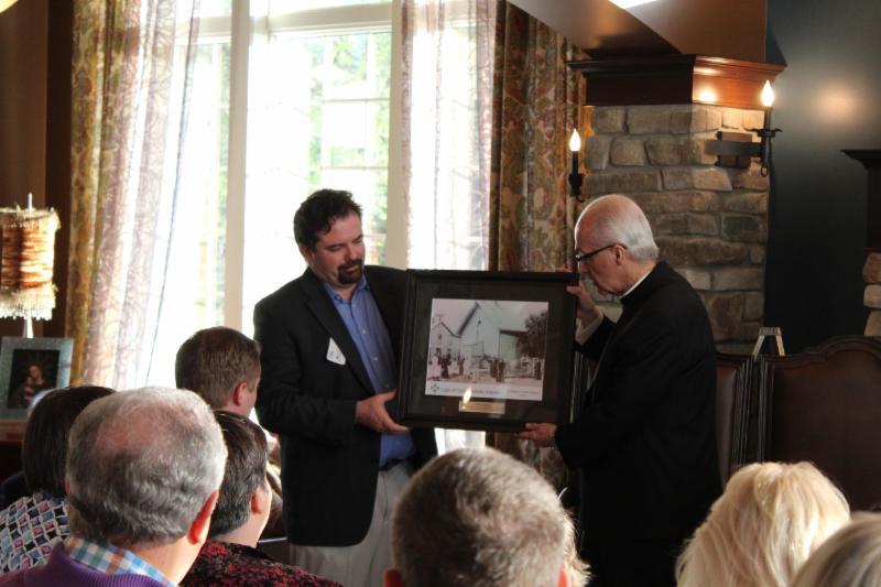 Light of Christ Mission Advancement Director Tim McCaffrey presented Bishop David Kagan with a framed photo of the first Catholic school in Bismarck, circa 1878.