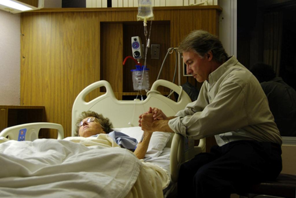 This man is a hospice worker holding the hand of a dying woman experiencing her last breaths. This man cares for others who are in the darkest of places, who himself must be wracked with pain.
