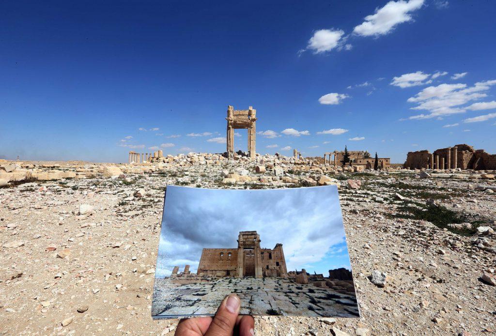 A photographer on March 31, 2016 holds a two-year-old photo of the Temple of Bel in front of the historic remains after the temple was destroyed by Islamic State jihadis in September 2015, in the