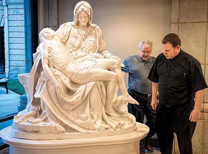 Father Adam Keiter and Pat Kerivan walk around a replica of Michelangelo s Pieta after it was set into place Tuesday morning in the gathering space of the Cathedral of the Immaculate Conception in