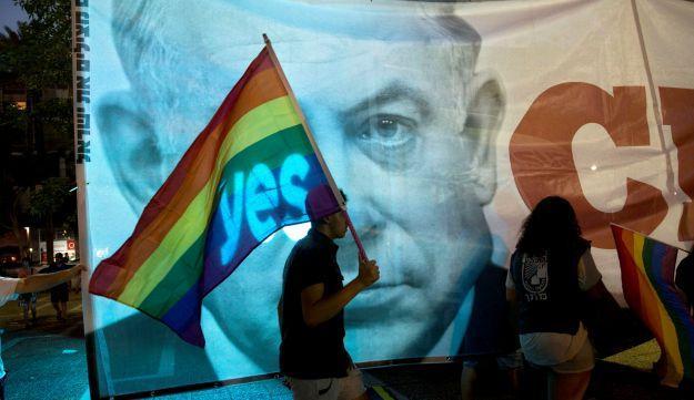 An Israeli walks with a flag in front of a banner showing Israeli Prime Minister Benjamin Netanyahu during a rally against inequality for the LGBT community in Tel Aviv, Israel.