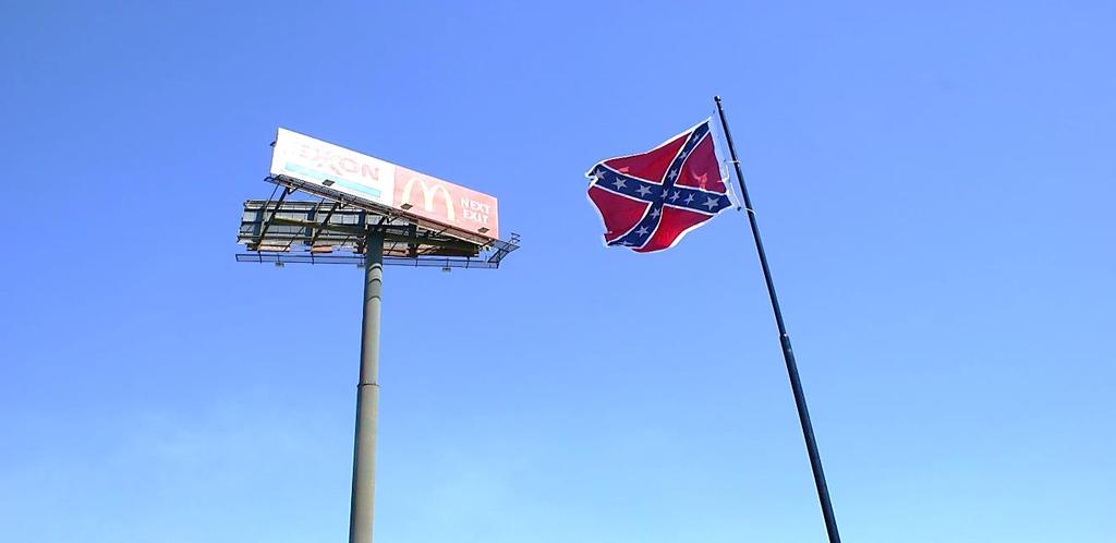 I saw was H. K. Edgerton standing beside frontage road across from the flag pole in his Confederate uniform and carrying a battle flag there was no doubt we were at the right spot.