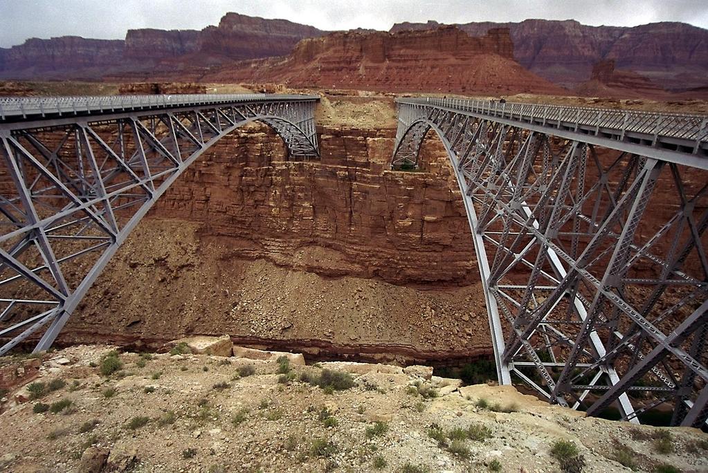 Arizona's Historic Navajo Bridge spans Marble Canyon in a graceful silvery arch approximately 470 ft. above the Colorado River. The original 1928 bridge that replaced Lee s Ferry is on the right.