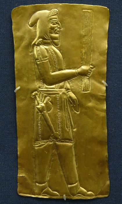 Note the cloak. For this author, this style of clothing identifies a possible magus here depicted carrying a barsom bundle and what may be a haoma cup. The magi are at times depicted carrying weapons.