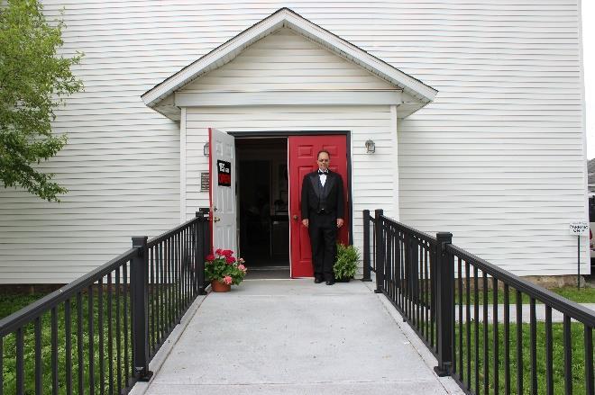 BRIGHTENING THE ENTRYWAY Notice President Roger Buschman standing in front or our cheery red door. Roger dressed in the tux to greet guests at our annual tea party.