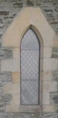Early thirteenth century style plate tracery single light bald lancet glazed window set in a flat headed truncated triangular headstone; stepped jamb stones externally and splayed external