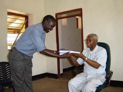 RECONCILE s Executive Director Emmanuel LoWilla presents Bishop Ghasi with a copy of the CPA.
