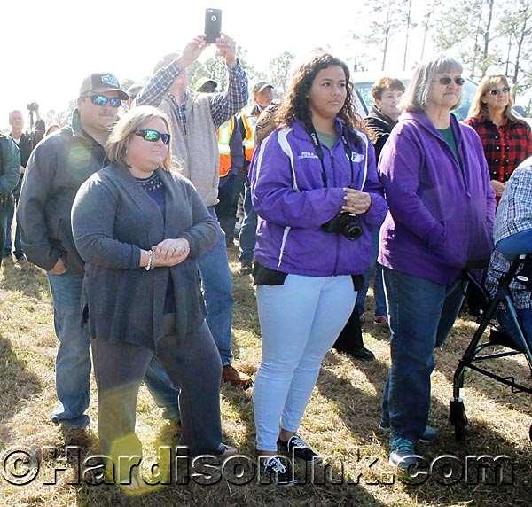 Brooke Ellzey Willis (in gray sweater at left) stands and listens during the